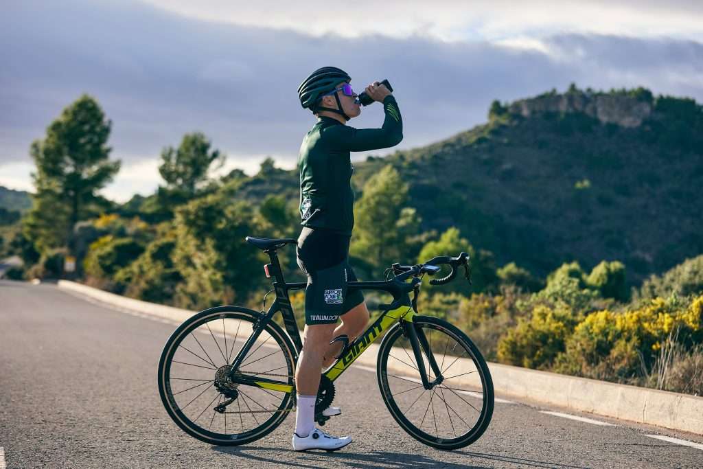 cyclist stood next to bike drinking from bottle