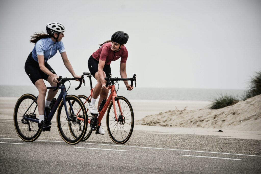 Discover how cycling can reduce the risks of dementia. Two cyclists pedal on a road by the beach, surrounded by a vibrant coastal landscape and clear blue skies