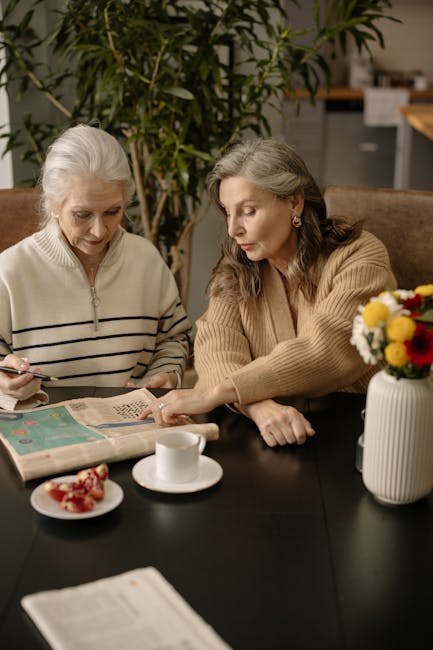 Two women seated at a table, engaged in reading a newspaper together.
